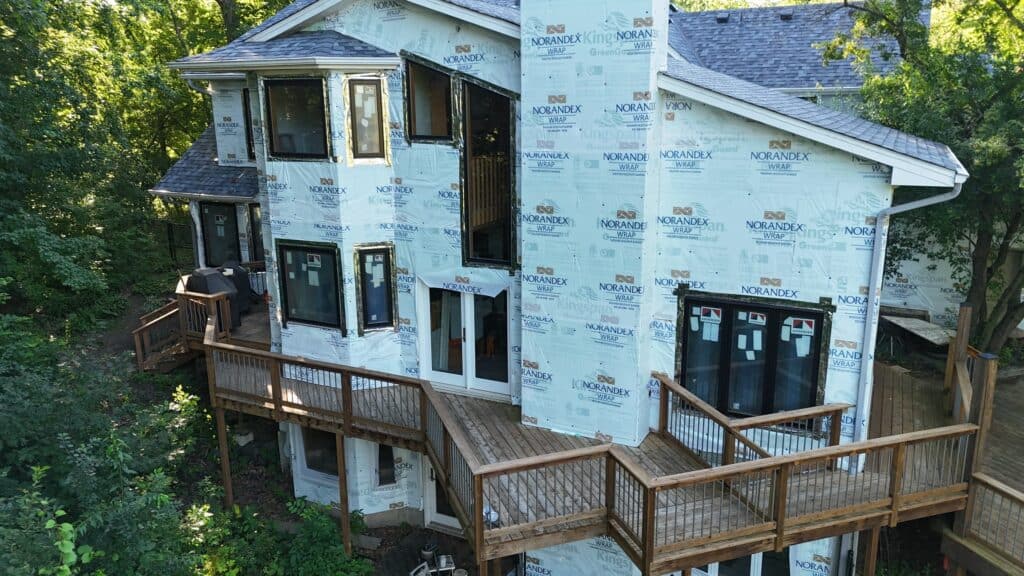 Window replacement Twin Cities – First Impressions Exteriors completing insurance-approved Andersen window replacement with new roof, siding, soffit, fascia, and gutters on White Bear Lake Minnesota home – aerial view during installation