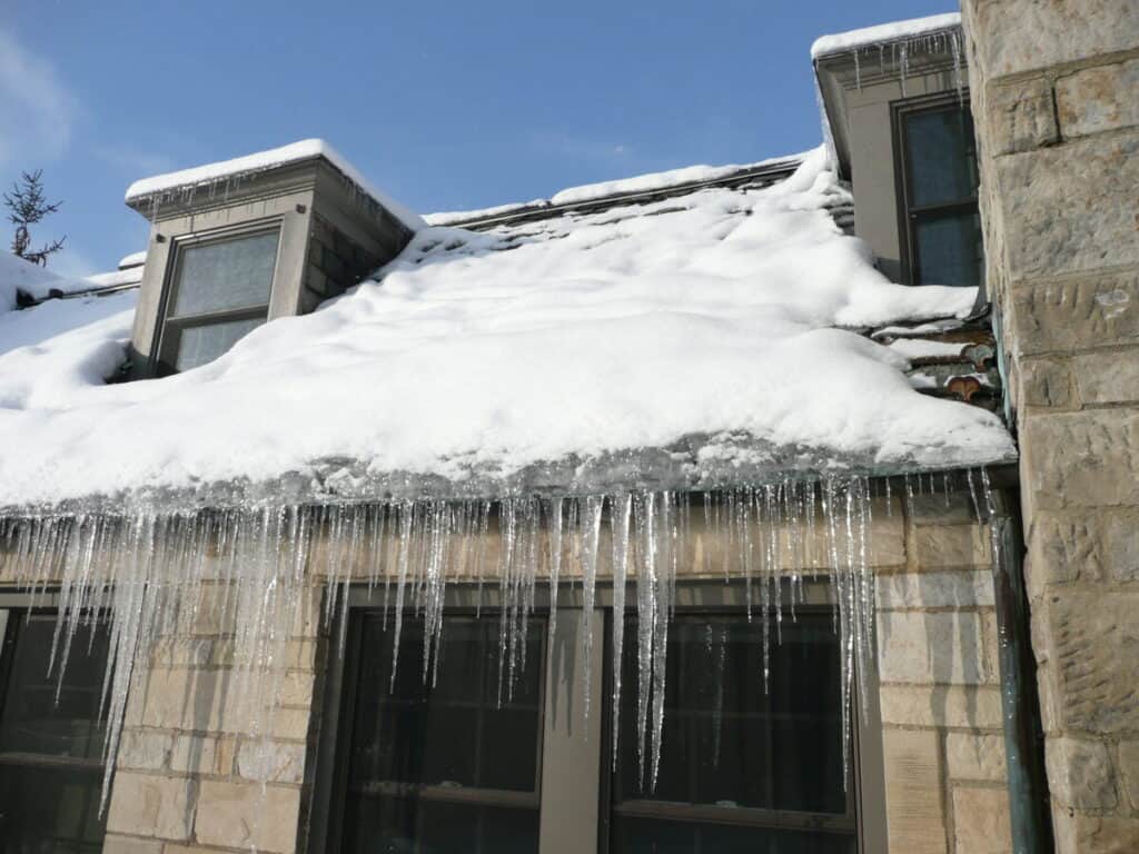 Ice dam with icicles along the eaves of a snow-covered residential roof