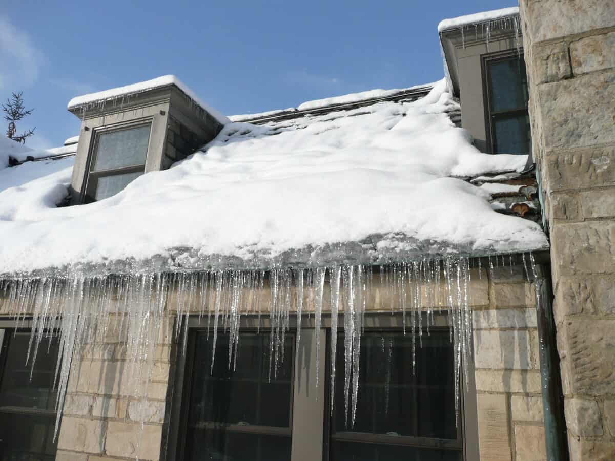 Ice dam with icicles along the eaves of a snow-covered residential roof