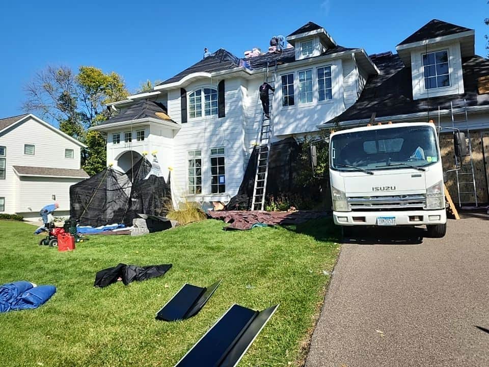 Crew working on a Minneapolis home exterior, with roof ladders and work truck